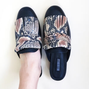 Zapatos tipo zuecos femeninos, de piel color negro, con detalle de “barbas” enfrente imitación animal print de serpiente que cubre todo el frente del zapato. Encima de esta pieza lleva una tira negra que pasa por lo ancho. Zapatos cómodos, sin tacón alto.