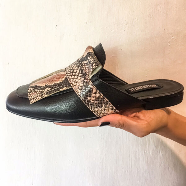 Zapatos tipo zuecos femeninos, de piel color negro, con detalle de “barbas” enfrente imitación animal print de serpiente que cubre todo el frente del zapato. Encima de esta pieza lleva una tira negra que pasa por lo ancho. Zapatos cómodos, sin tacón alto.
