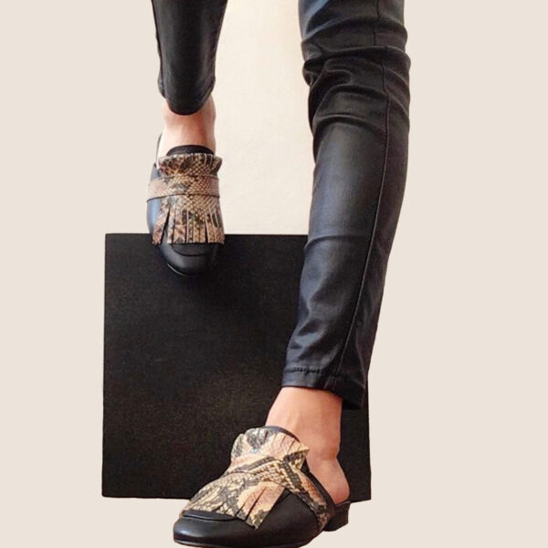 Zapatos tipo zuecos femeninos, de piel color negro, con detalle de “barbas” enfrente imitación animal print de serpiente que cubre todo el frente del zapato. Encima de esta pieza lleva una tira negra que pasa por lo ancho. Zapatos cómodos, sin tacón alto.