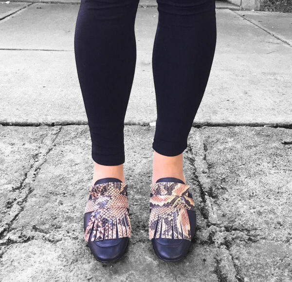 Zapatos tipo zuecos femeninos, de piel color negro, con detalle de “barbas” enfrente imitación animal print de serpiente que cubre todo el frente del zapato. Encima de esta pieza lleva una tira negra que pasa por lo ancho. Zapatos cómodos, sin tacón alto.