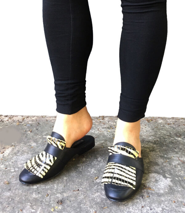 Zapatos tipo zuecos femeninos, de piel color negro, con detalle de “barbas” enfrente de animal print de zebra(color amarillo con negro) que cubre todo el frente del zapato. Encima de esta pieza lleva una tira negra que pasa por lo ancho. Zapatos cómodos, sin tacón alto.